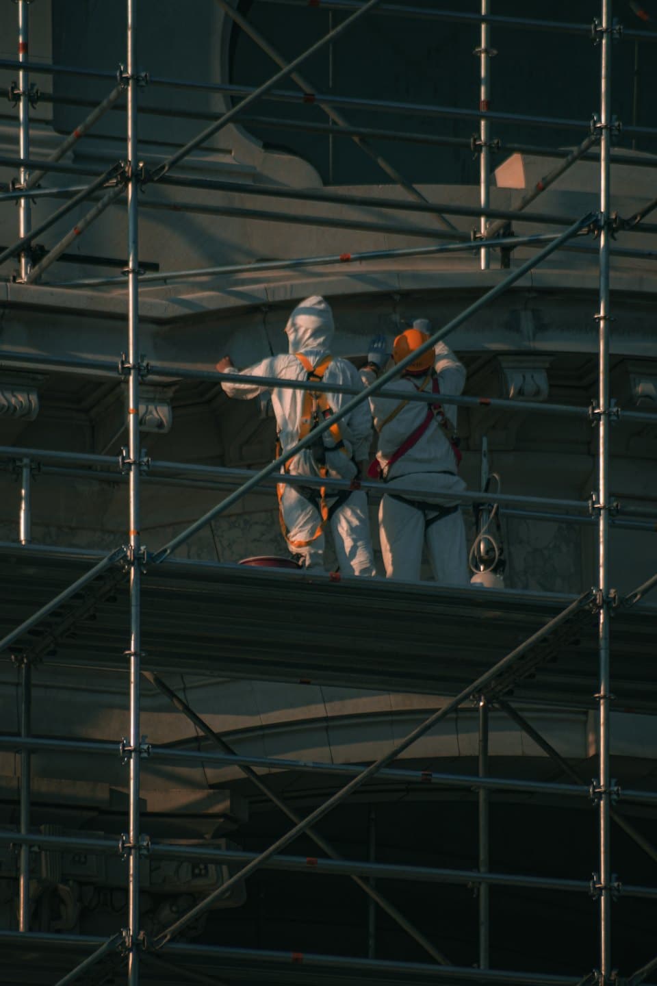 Operai in tute protettive su ponteggi riparano la facciata di un edificio in pietra.